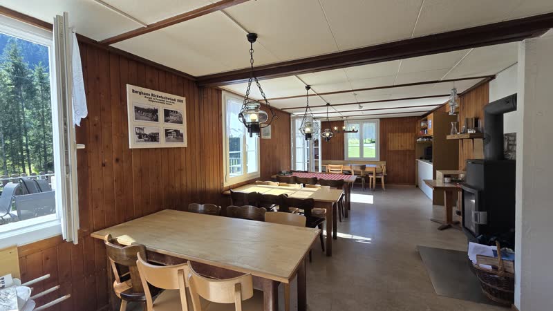 Gaststube mit holzgetäferten Wänden, langen Tischen, Stühlen und Hängelampen