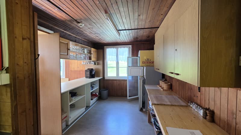 Küche mit Holzdecke, Schränken, Kühlschrank und Fenster zum Wald