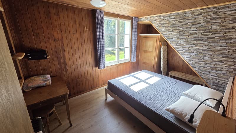 Lehrerzimmer mit Doppelbett, Schreibtisch, Natursteinwand und Fenster ins Grüne