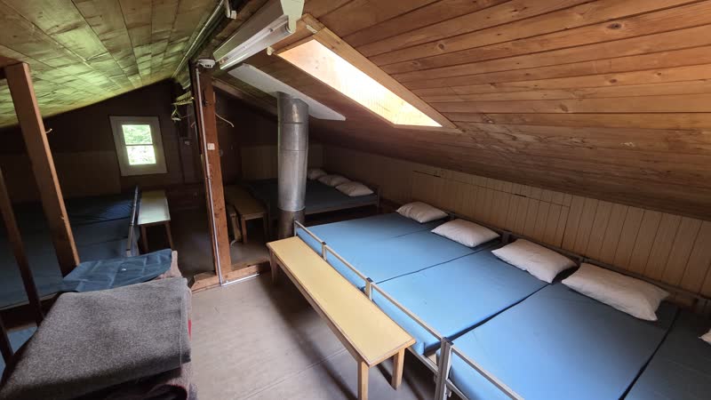 Dachstockzimmer mit Matratzenlager unter dem Holzdach, Dachfenster und Sitzbank