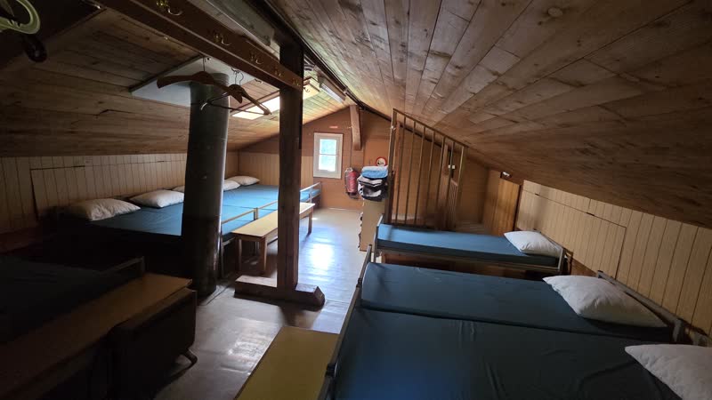 Dachstockzimmer mit mehreren Betten unter der Dachschräge und Kaminrohr